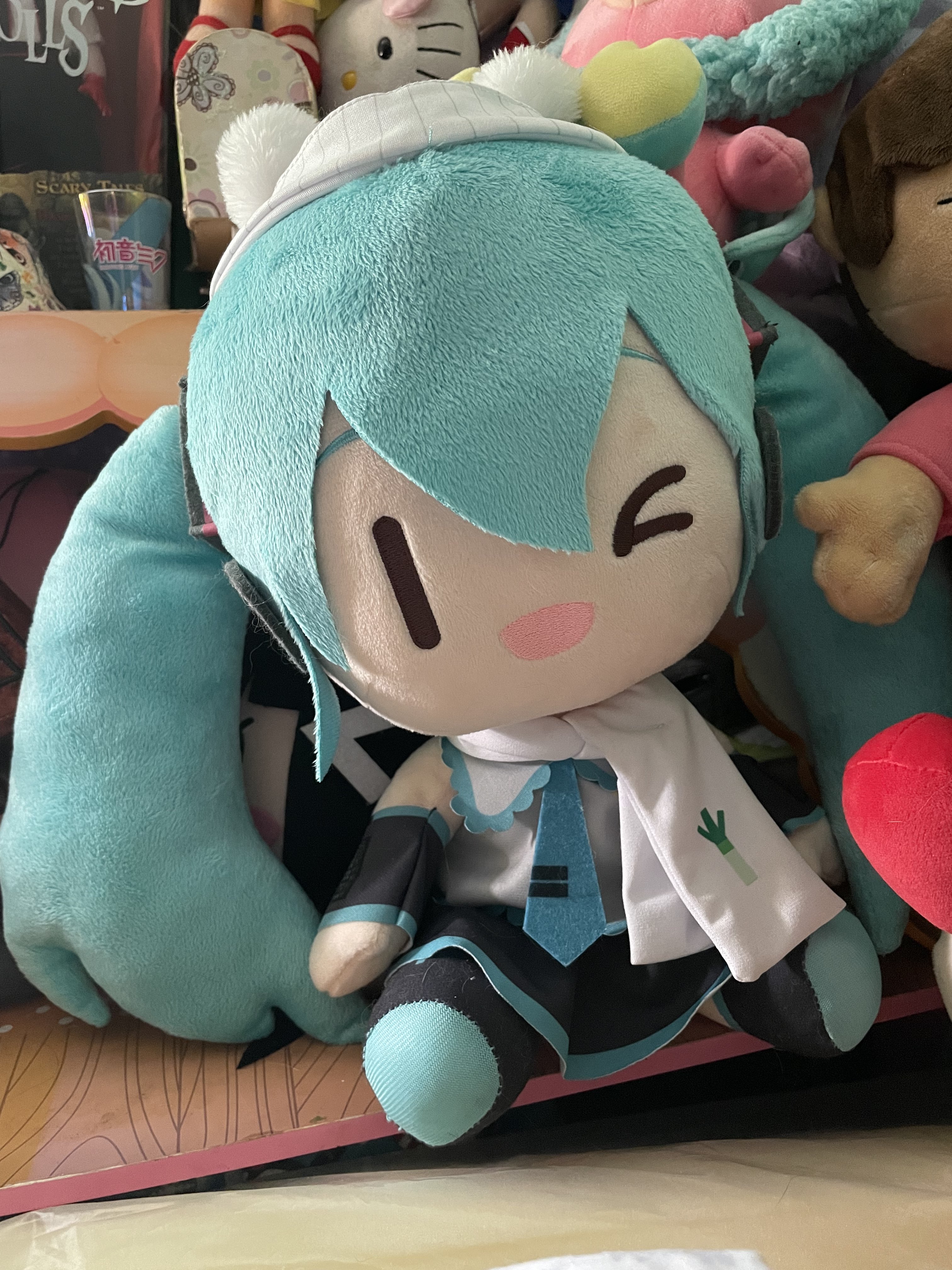 Large Miku plush wearing a scarf and a winter hat.